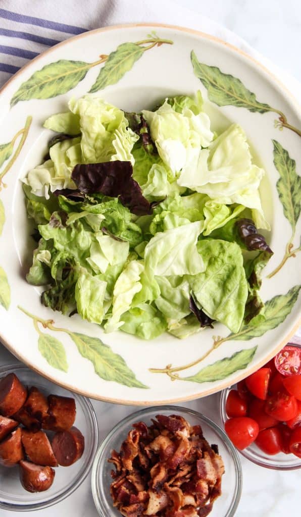 bowls of butter lettuce, hotdogs, bacon and tomatoes for salad