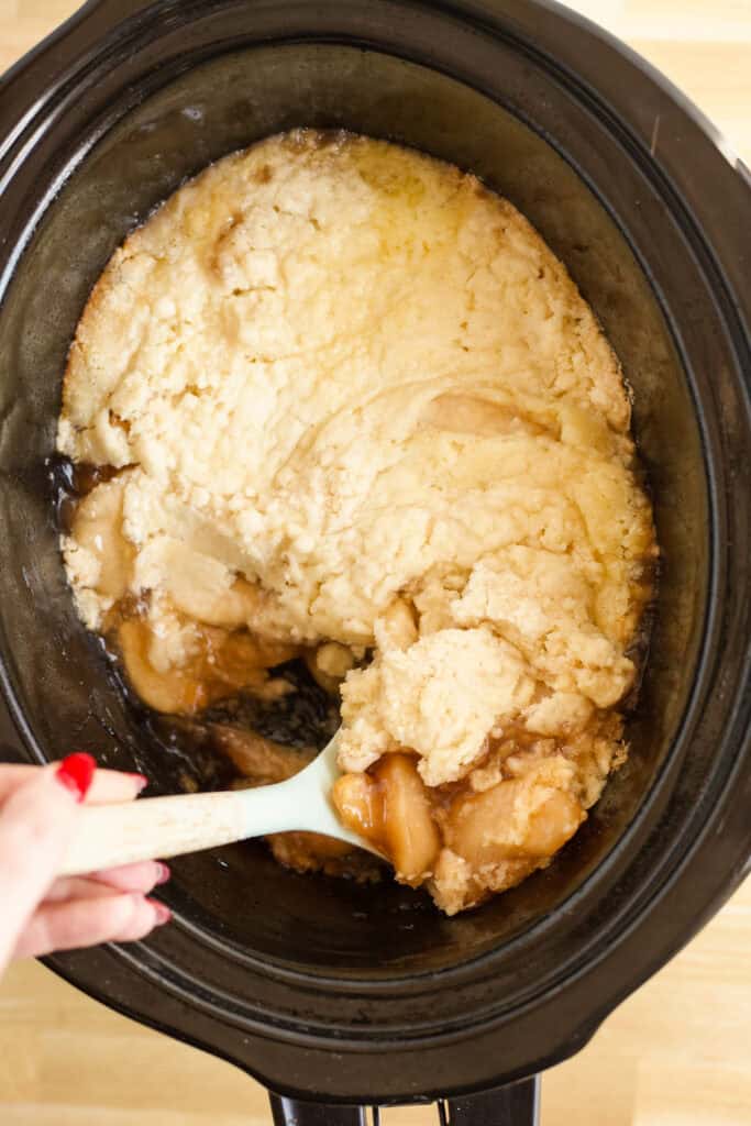 A hand scooping up a serving of apple dump cake.