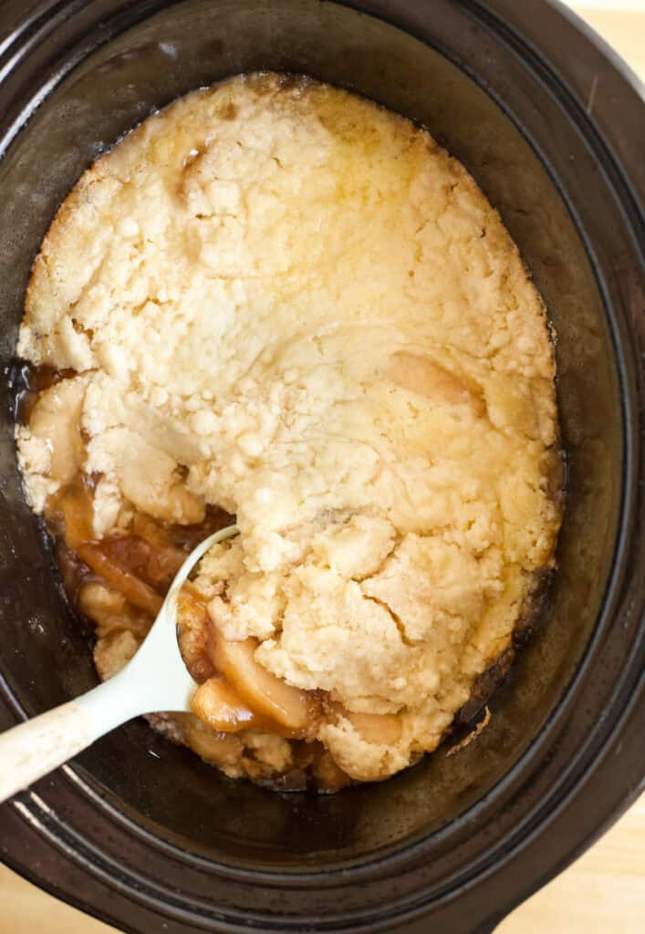 A spoon scooping up apple pie filling and yellow cake.