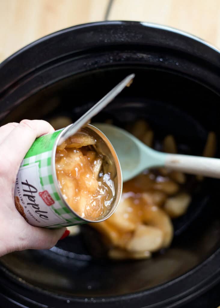 Apple pie filling being dumped into the bottom of a crockpot.