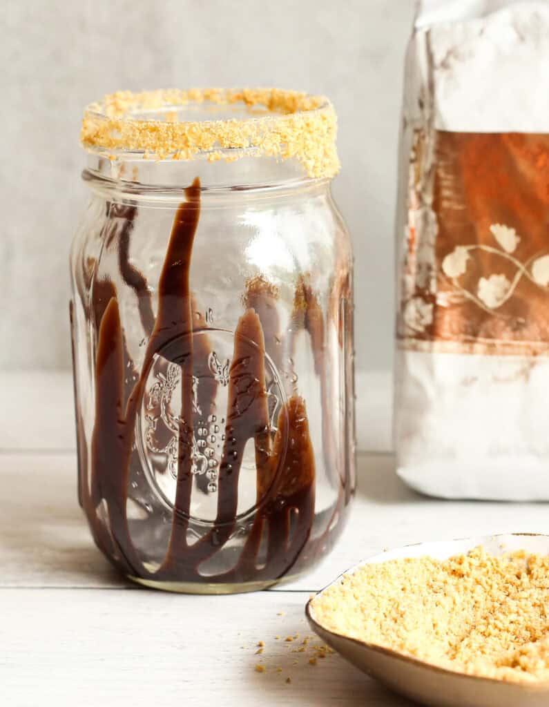 Glass jar drizzled with chocolate syrup and topped with crushed graham crackers.