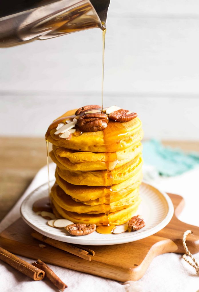 syrup being poured over a stack of pumpkin pancakes