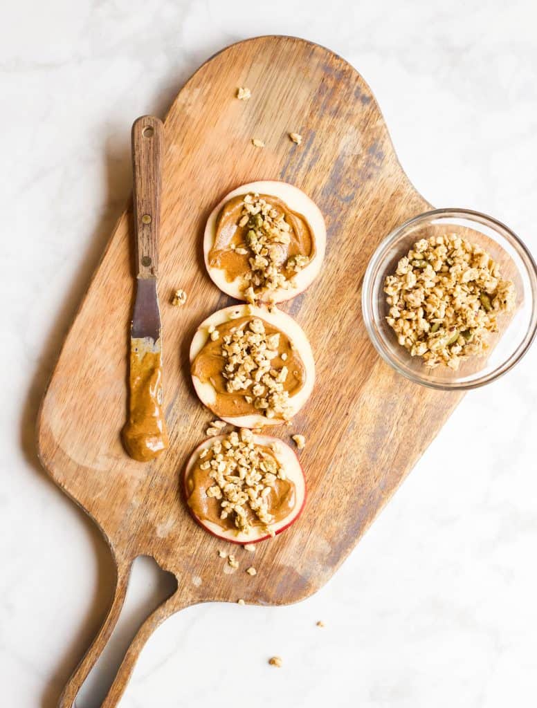apple slices with nut butter and granola on a board