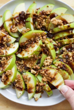 hand taking a slice of apple from a plate of apple nachos