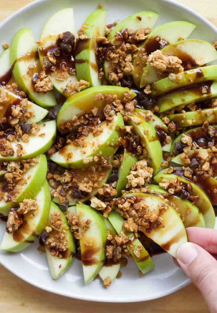 hand taking a slice of apple from a plate of apple nachos