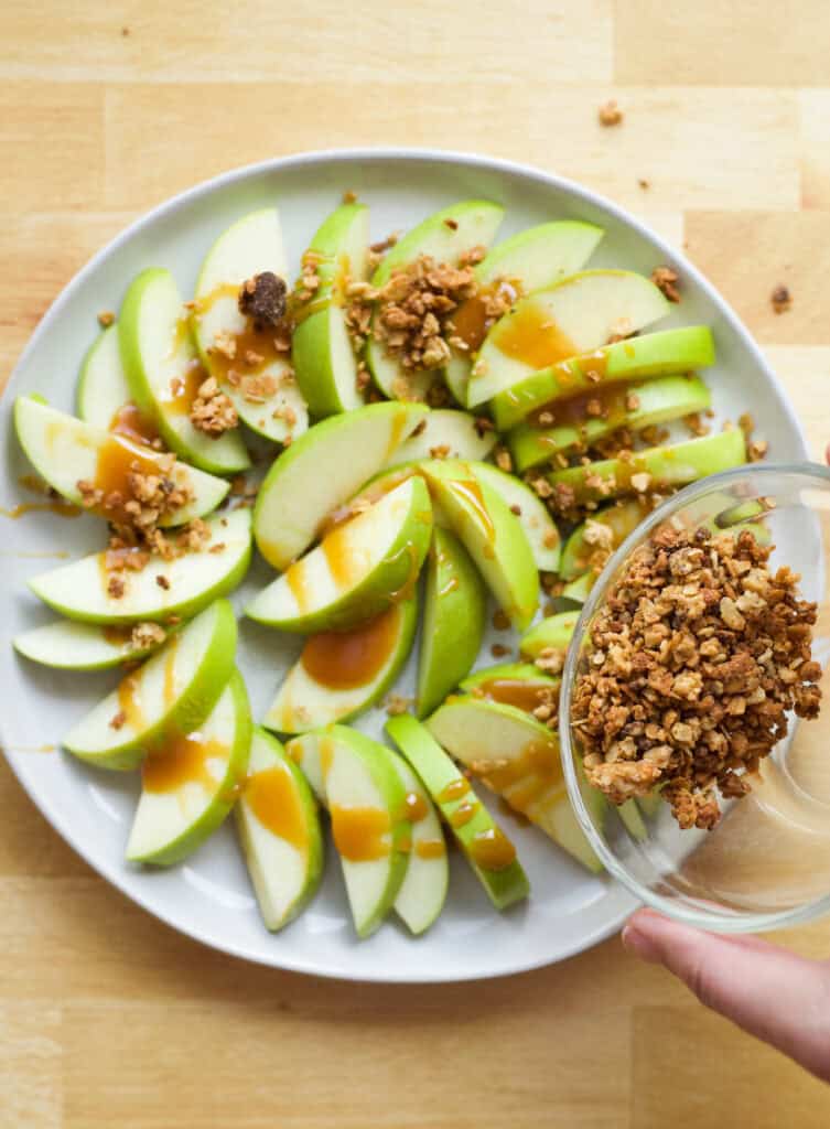 sprinkling granola onto caramel apple slices