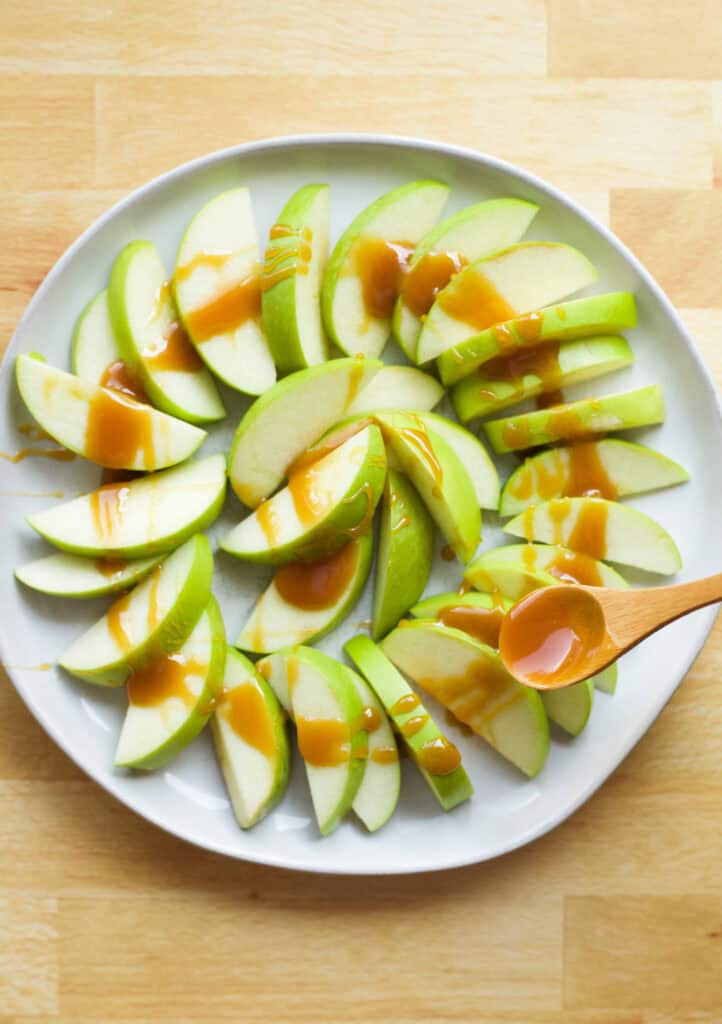 using a spoon to drizzle caramel sauce onto apple slices