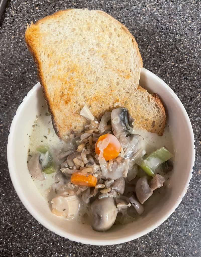piece of sourdough toast in a bowl of mushroom chicken and wild rice soup