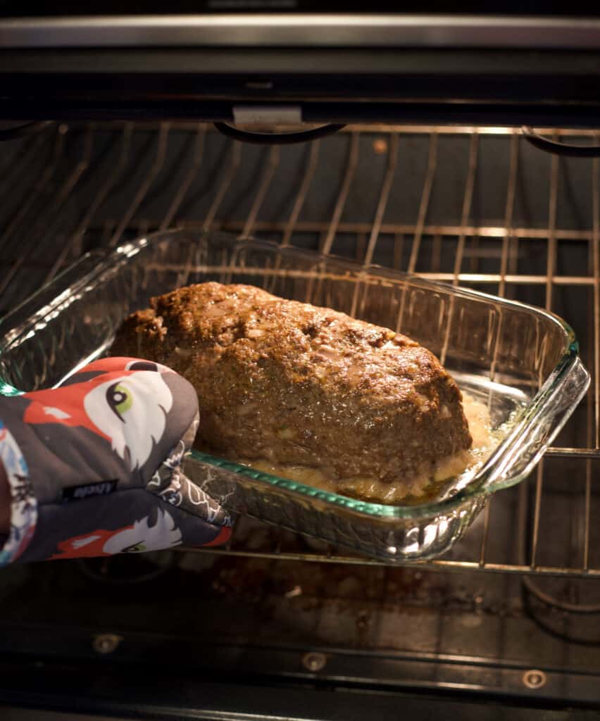 hand removing a pan with a meatloaf from the oven