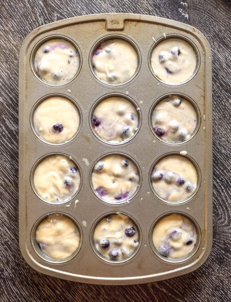 Blueberry muffin batter scooped into a muffin tin.