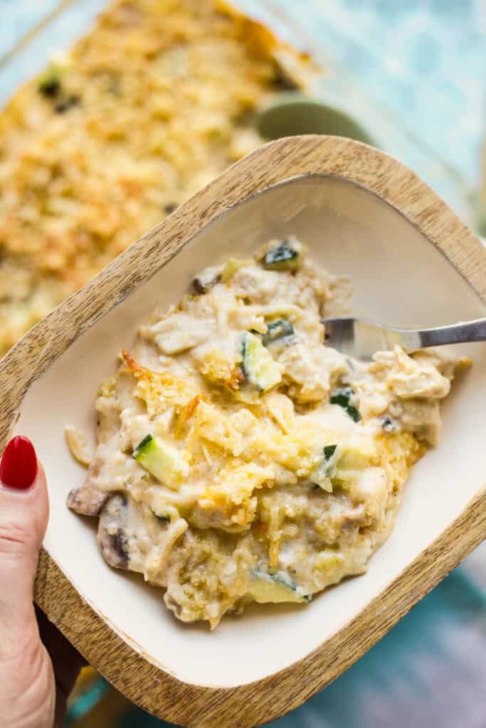 Hand holding bowl with a serving of creamy Million Dollar Chicken Spaghetti casserole.