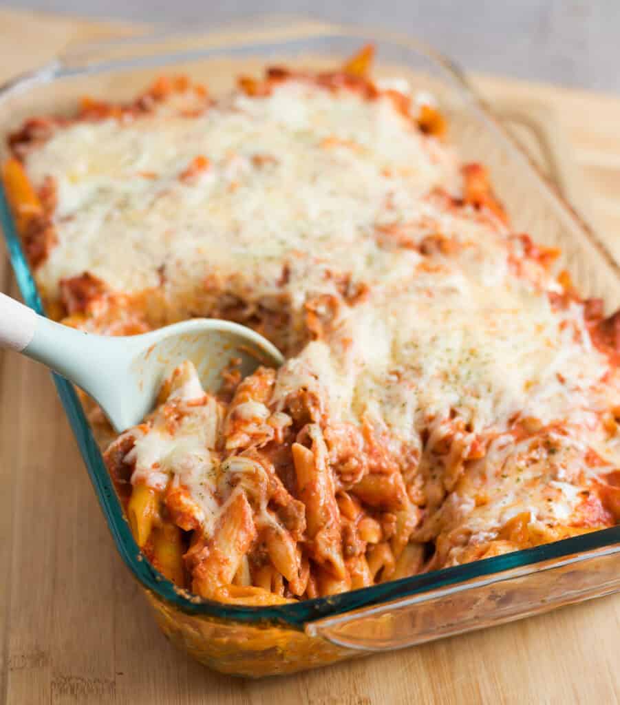 Big spoon scooping up a portion of cheesy Baked Penne with Vodka Sauce.