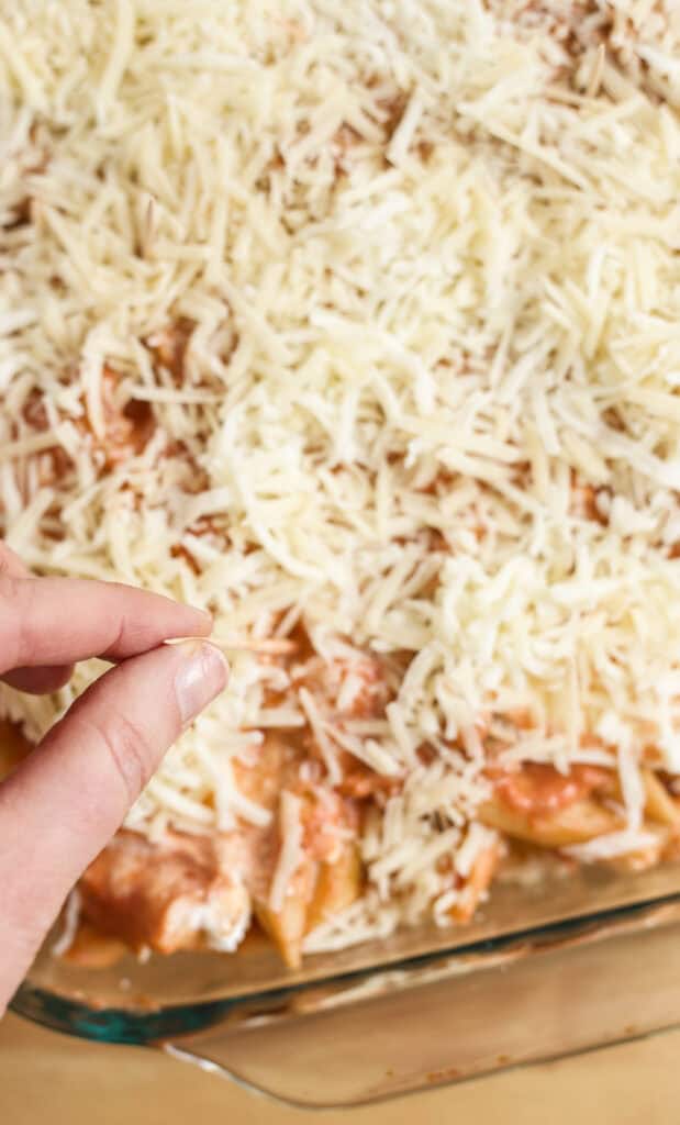 Hand placing toothpick in unbaked Penne with Vodka Sauce.